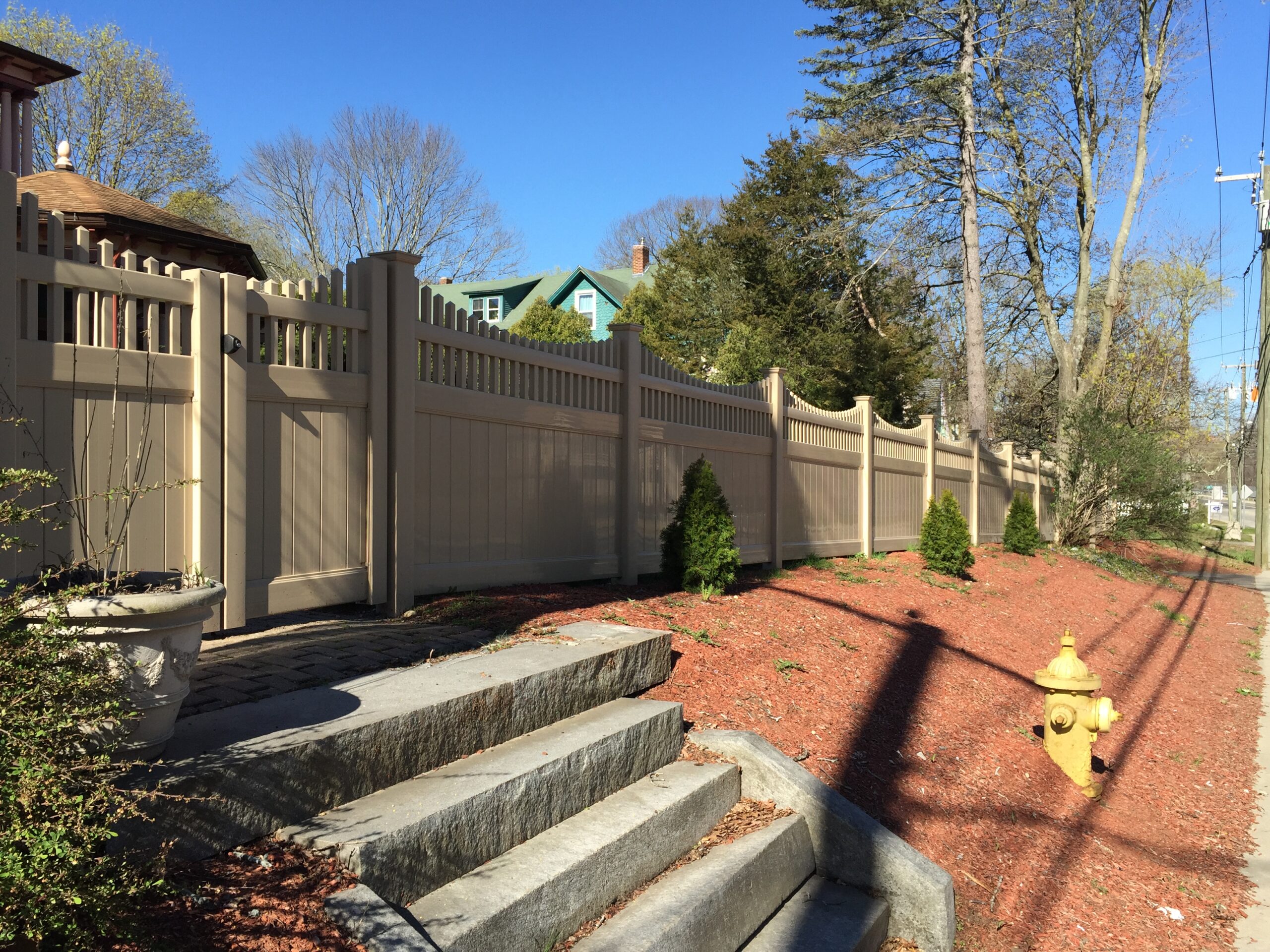 Tan vinyl privacy fence running along a sidewalk in a Connecticut neighborhood