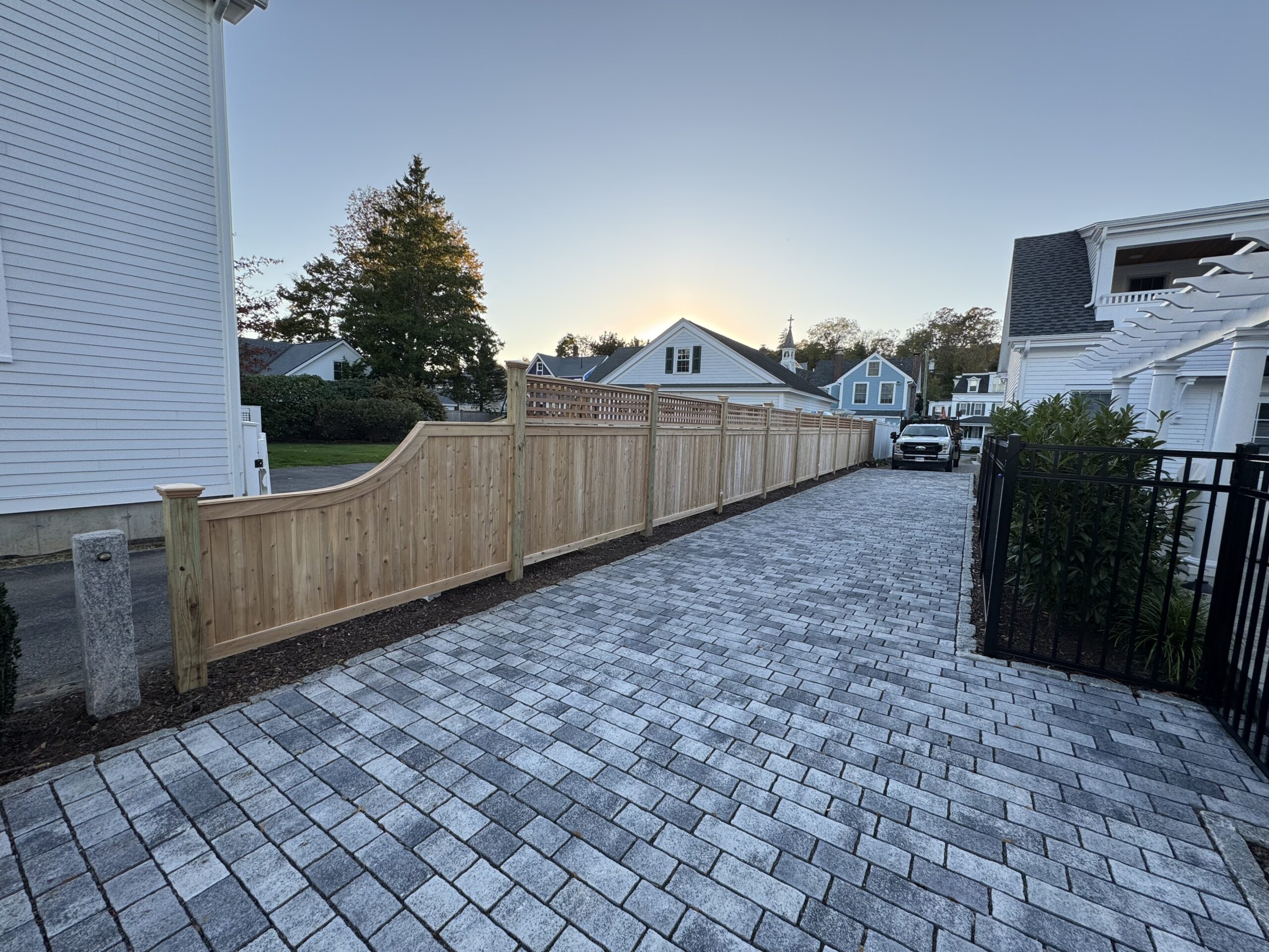 Unstained cedar privacy fence with scalloped lattice top along a paver driveway in Connecticut