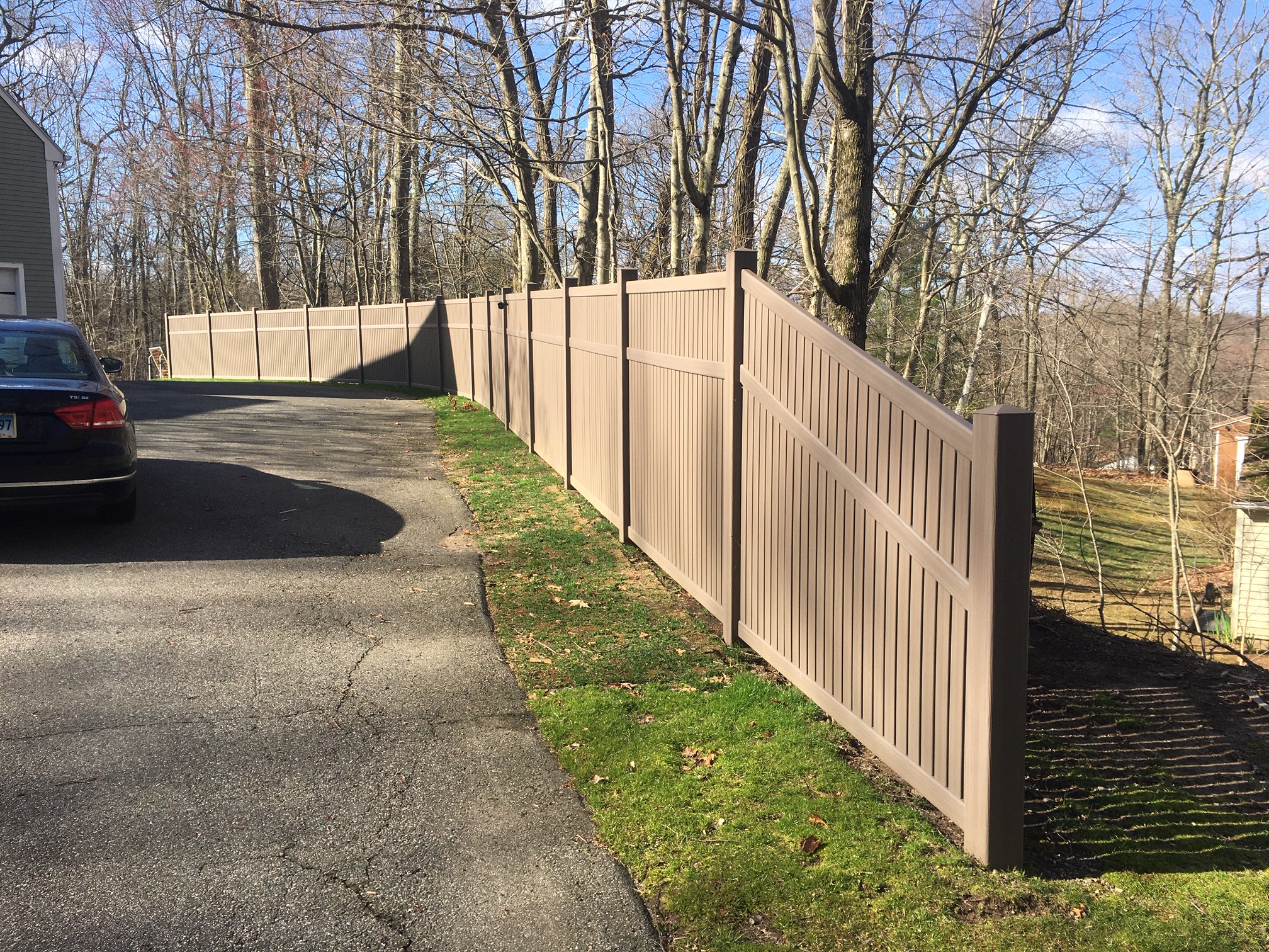 Tan vinyl privacy fence along a residential driveway in Connecticut
